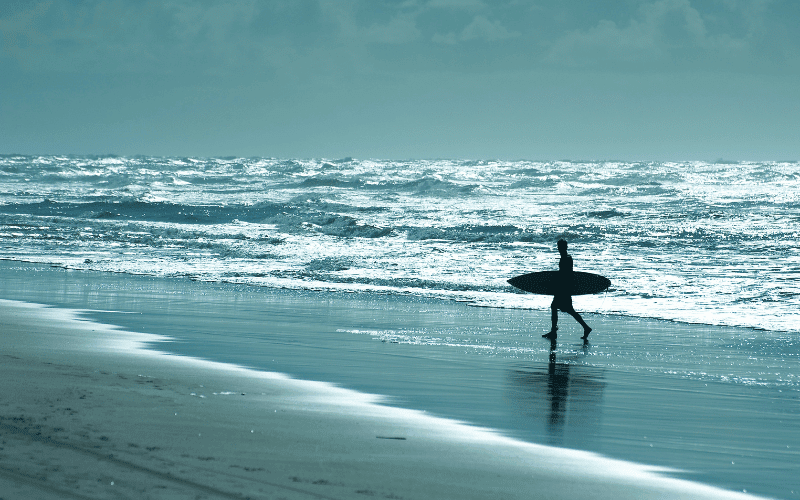 A beginner surfer practices basic techniques on a calm, sunny beach with a clear blue sky and gentle waves